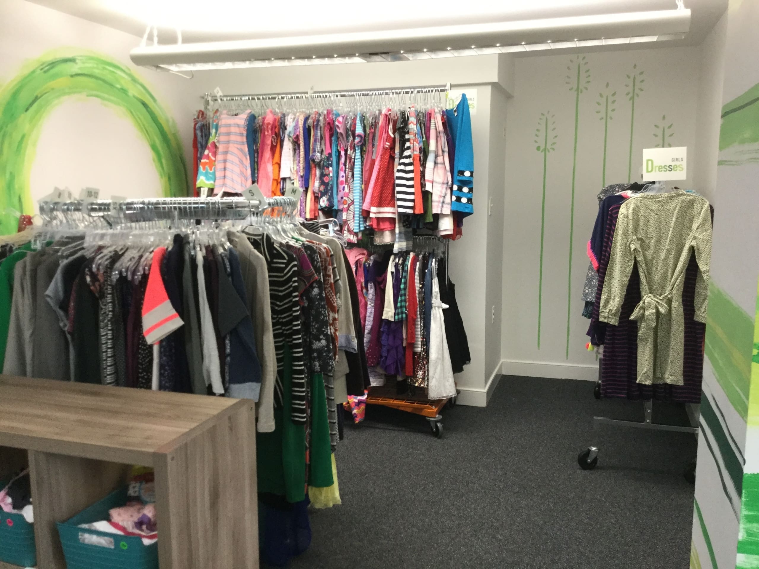 Clothing racks filled with children's dresses and jackets in a community store.