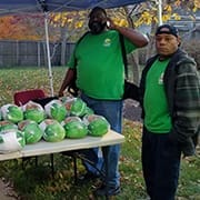 Two men standing by a table with food donations during a community outreach event