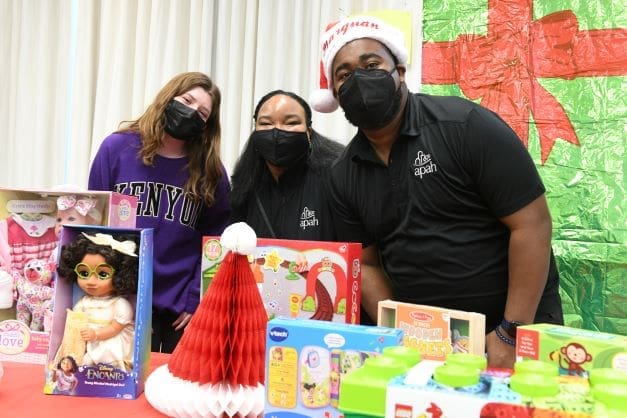 Three people posing for a photo wearing masks, toys on the table.