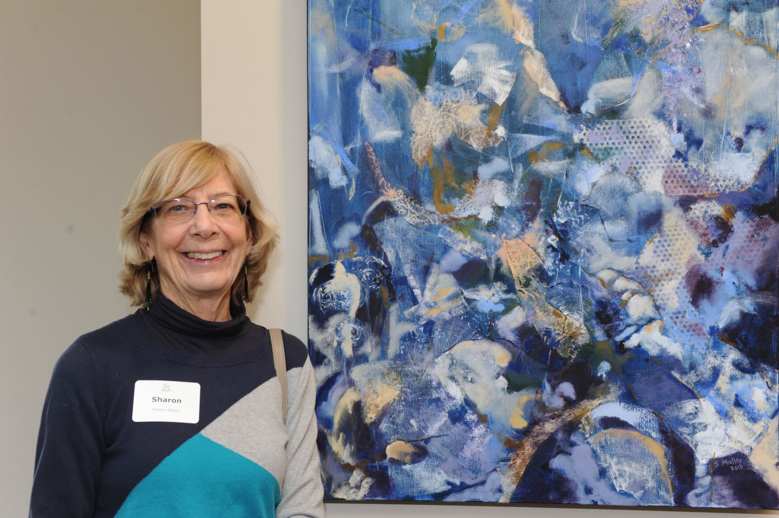 A woman named Sharon standing beside an abstract blue art piece.