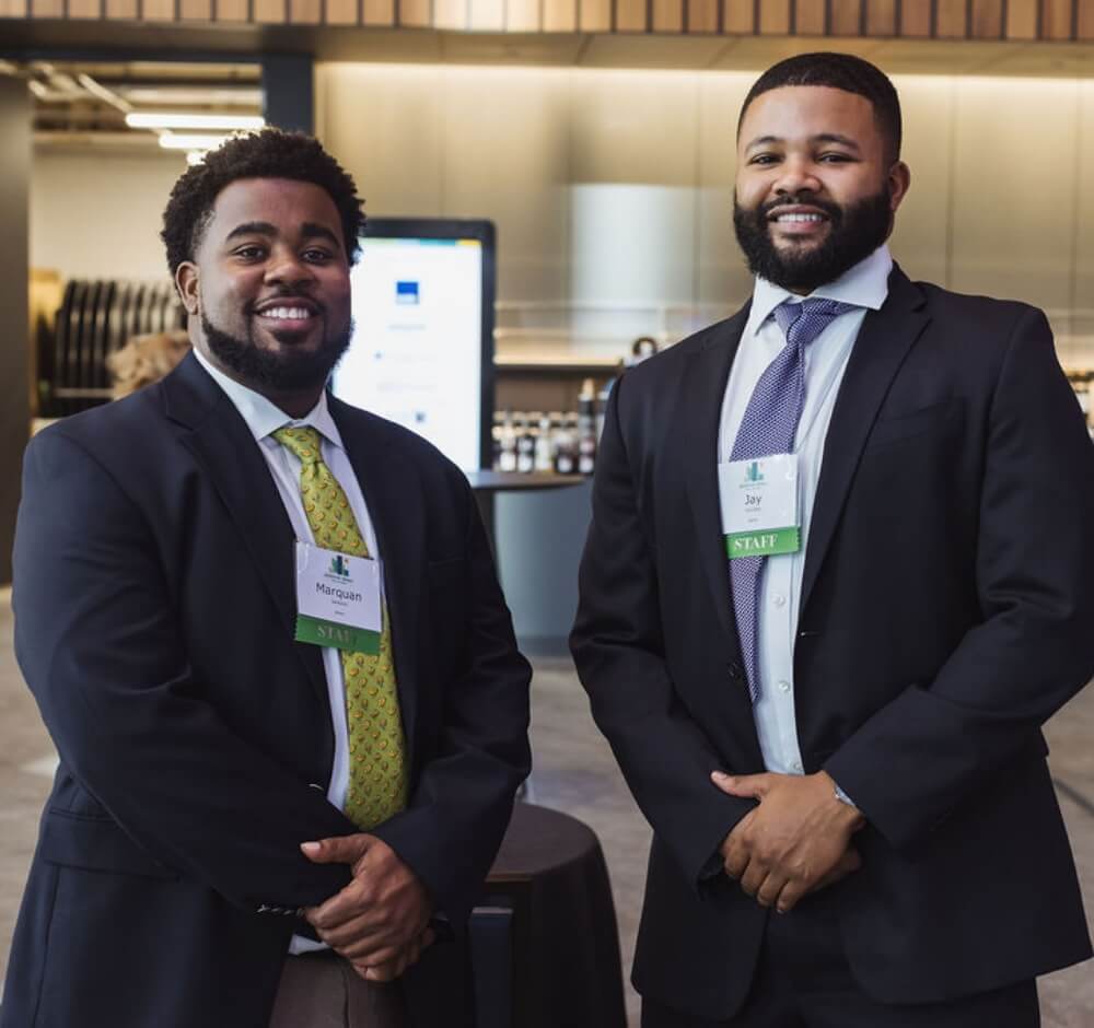 Two men in suits smiling at a professional event, wearing staff badges