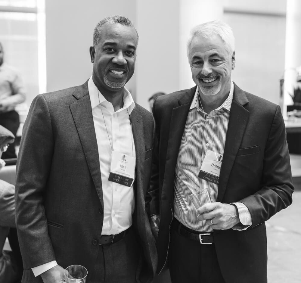True-Ground-Partner-with-Residents-Services-Partner-with-Us@2x Two men in business attire smiling at a networking event